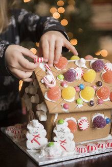 Hände eines kaukasischen Mädchens beim Verzieren eines Lebkuchenhauses mit Süßigkeiten - BLEF01814