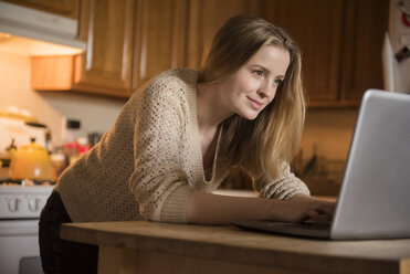 Smiling woman using laptop in domestic kitchen - BLEF01825