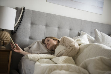 Woman laying in bed texting on cell phone - BLEF01826