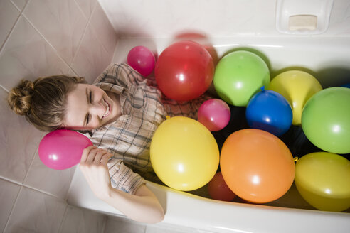 Lächelnde Frau in der Badewanne sitzend mit bunten Luftballons - BLEF01834