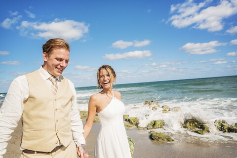 Kaukasische Braut und Bräutigam halten Hände am Strand, lizenzfreies Stockfoto