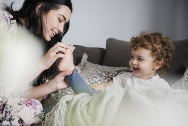 Caucasian mother sitting on sofa playing with toes of son - BLEF01907