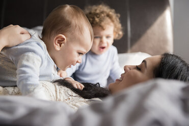 Kaukasische Mutter liegt auf dem Bett und spielt mit ihren Söhnen - BLEF01920