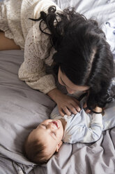 Caucasian mother laying on bed tickling baby son - BLEF01927