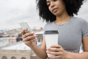 Afroamerikanische Frau trinkt Kaffee und schreibt eine SMS mit dem Handy - BLEF01943