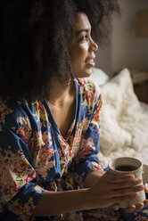 Afroamerikanische Frau sitzt im Bett und trinkt Kaffee - BLEF01947