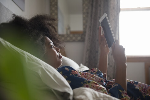 Afroamerikanische Frau liegt im Bett und liest auf einem digitalen Tablet - BLEF01950