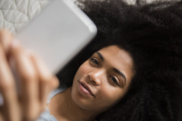Afroamerikanische Frau liegt im Bett und schreibt eine SMS auf ihrem Handy - BLEF01953