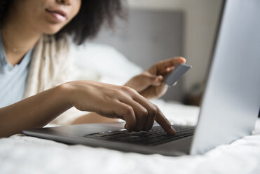 Im Bett liegende afroamerikanische Frau beim Online-Shopping mit Laptop - BLEF01955