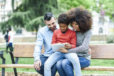 Family sitting on a park bench, using digital tablet - JSMF01053