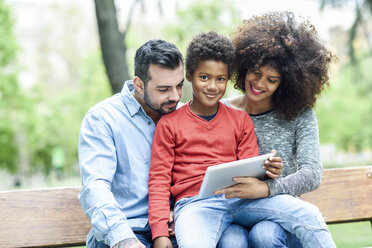 Familie sitzt auf einer Parkbank und benutzt ein digitales Tablet - JSMF01054