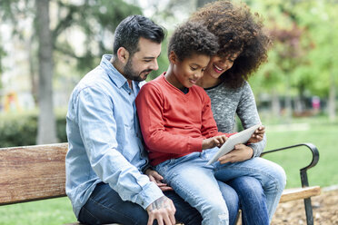 Familie sitzt auf einer Parkbank und benutzt ein digitales Tablet - JSMF01055