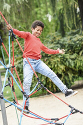 Little boy playing on playground in a park, climbing in a jungle gym - JSMF01061