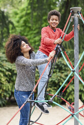 Mutter und Sohn spielen auf einem Spielplatz in einem Park und klettern auf einem Klettergerüst - JSMF01062