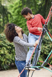 Mother and son playing on playground in a park, climbing in a jungle gym - JSMF01063