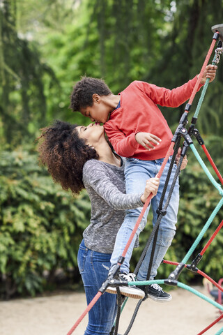 Mutter und Sohn spielen auf einem Spielplatz in einem Park und klettern auf einem Klettergerüst, lizenzfreies Stockfoto