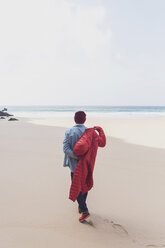 Portugal, Algarve, Sagres, Praia do Beliche, Rückansicht eines Mannes, der am Strand spazieren geht und seine Jacke anzieht - MMAF00880