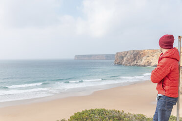 Portugal, Algarve, Sagres, Praia do Beliche, Mann mit roter Mütze und Jacke schaut auf den Strand und das Meer - MMAF00883