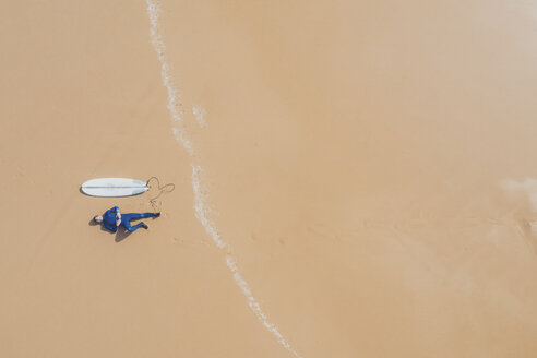 Portugal, Algarve, Sagres, Praia da Mareta, aerial view of man lying next to surfboard on the beach - MMAF00899