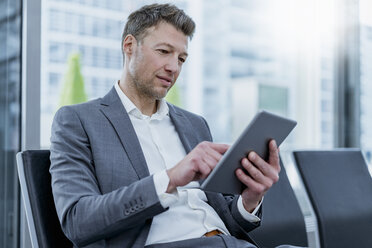 Businessman sitting in waiting area using tablet - DIGF06827