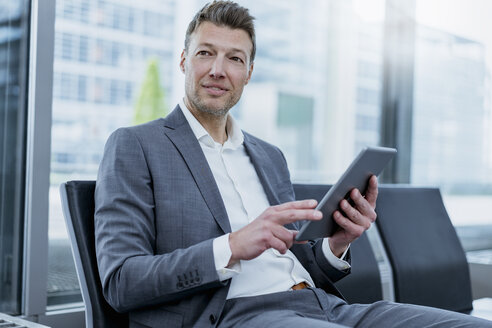 Businessman sitting in waiting area using tablet - DIGF06828