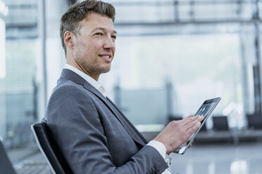 Businessman sitting in waiting area using tablet - DIGF06829