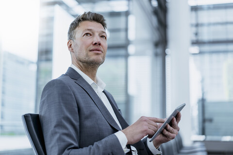 Geschäftsmann sitzt im Wartebereich und benutzt ein Tablet, lizenzfreies Stockfoto