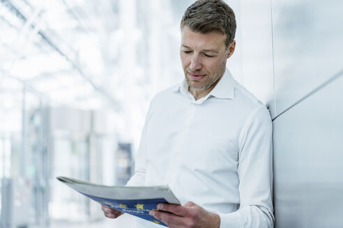 Businessman leaning against a wall reading newspaper - DIGF06834