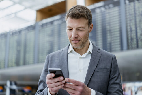 Porträt eines Geschäftsmannes, der auf dem Flughafen ein Mobiltelefon benutzt - DIGF06839