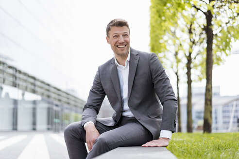 Happy businessman sitting outside in the city - DIGF06841