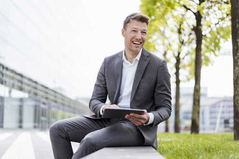 Happy businessman with tablet sitting outside in the city - DIGF06842