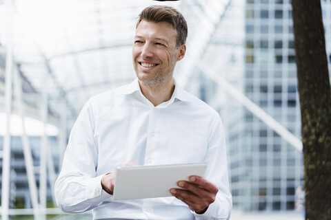 Lächelnder Geschäftsmann mit Tablet draußen in der Stadt, lizenzfreies Stockfoto