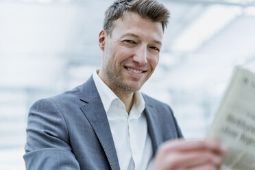 Portrait of smiling businessman reading newspaper - DIGF06864