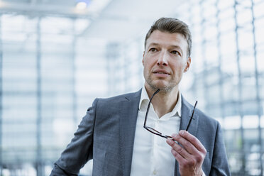 Portrait of businessman holding glasses looking around - DIGF06866