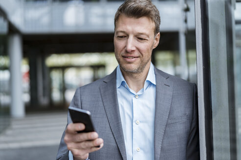 Portrait of businessman looking at cell phone outdoors - DIGF06891