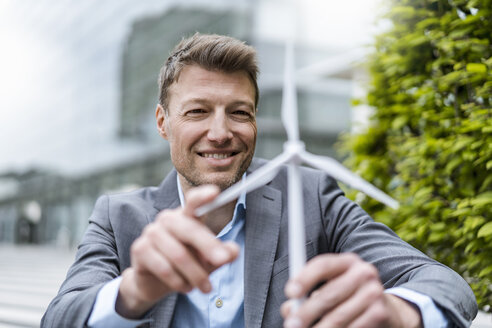 Businessman with wind turbine model outdoors - DIGF06894