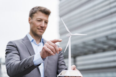 Businessman with wind turbine model outdoors - DIGF06896