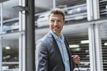 Porträt eines lächelnden Geschäftsmannes auf einem Parkplatz, der sich umschaut - DIGF06898