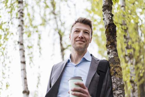Smiling businessman with takeaway coffee in a park - DIGF06908