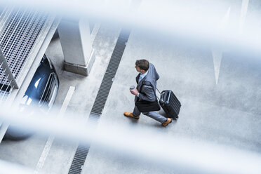 Top view of businessman walking with baggage and takeaway coffee at a car park - DIGF06912