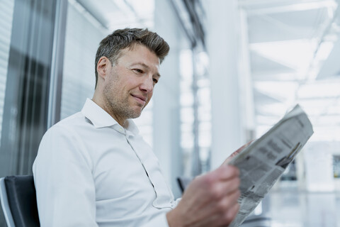 Geschäftsmann sitzt im Wartebereich und liest Zeitung, lizenzfreies Stockfoto