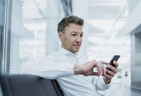 Businessman sitting in waiting area using cell phone stock photo