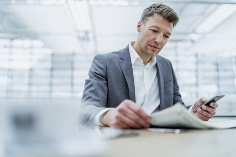 Businessman with cell phone reading newspaper in a cafe stock photo