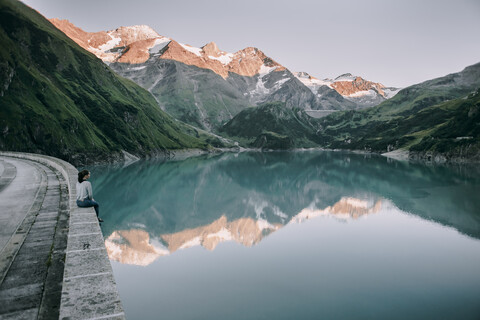 Kaukasische Frau sitzt auf einer Mauer am Bergsee, lizenzfreies Stockfoto