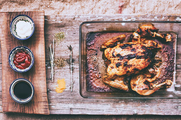 Nahaufnahme von gebratenem Huhn mit Rosmarin und Soßen auf Holztisch - BLEF02055