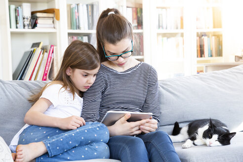 Zwei Schwestern sitzen zu Hause auf der Couch und schauen einen Film mit einem digitalen Tablet - LVF08009