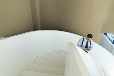 Geschäftsmann benutzt Mobiltelefon auf einer Treppe in einem modernen Büro - AHSF00209