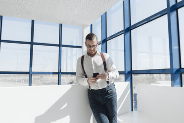 Businessman using cell phone at the window in modern office - AHSF00212