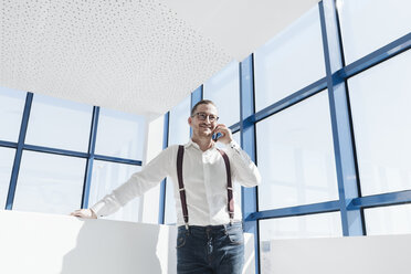 Geschäftsmann im Gespräch mit Handy am Fenster in einem modernen Büro - AHSF00215