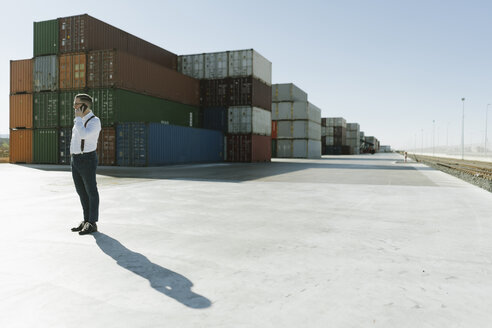 Manager, der vor Frachtcontainern auf einem Industriegelände mit seinem Handy telefoniert - AHSF00217